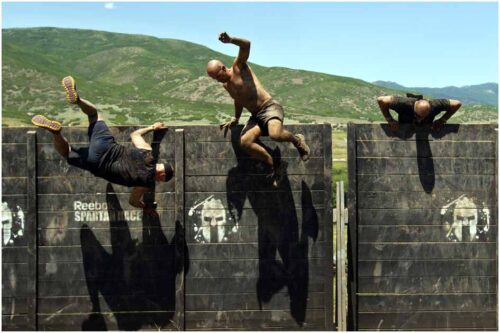 Chris Detrick | The Salt Lake Tribune Competitors jump over an 8-foot wall during the Utah Spartan Beast Race at Soldier Hollow Saturday June 29, 2013. The 12-mile race included obstacles like mud pits with barbed wire, rope climbs, jumping over fire and climbing an eight-foot wall.